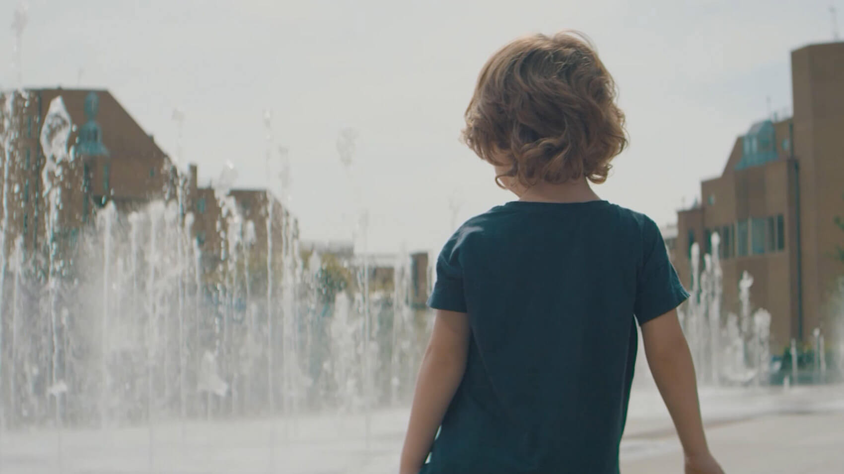 A boy plays in fountains in a still from a property video production by Spaces and Rise Media