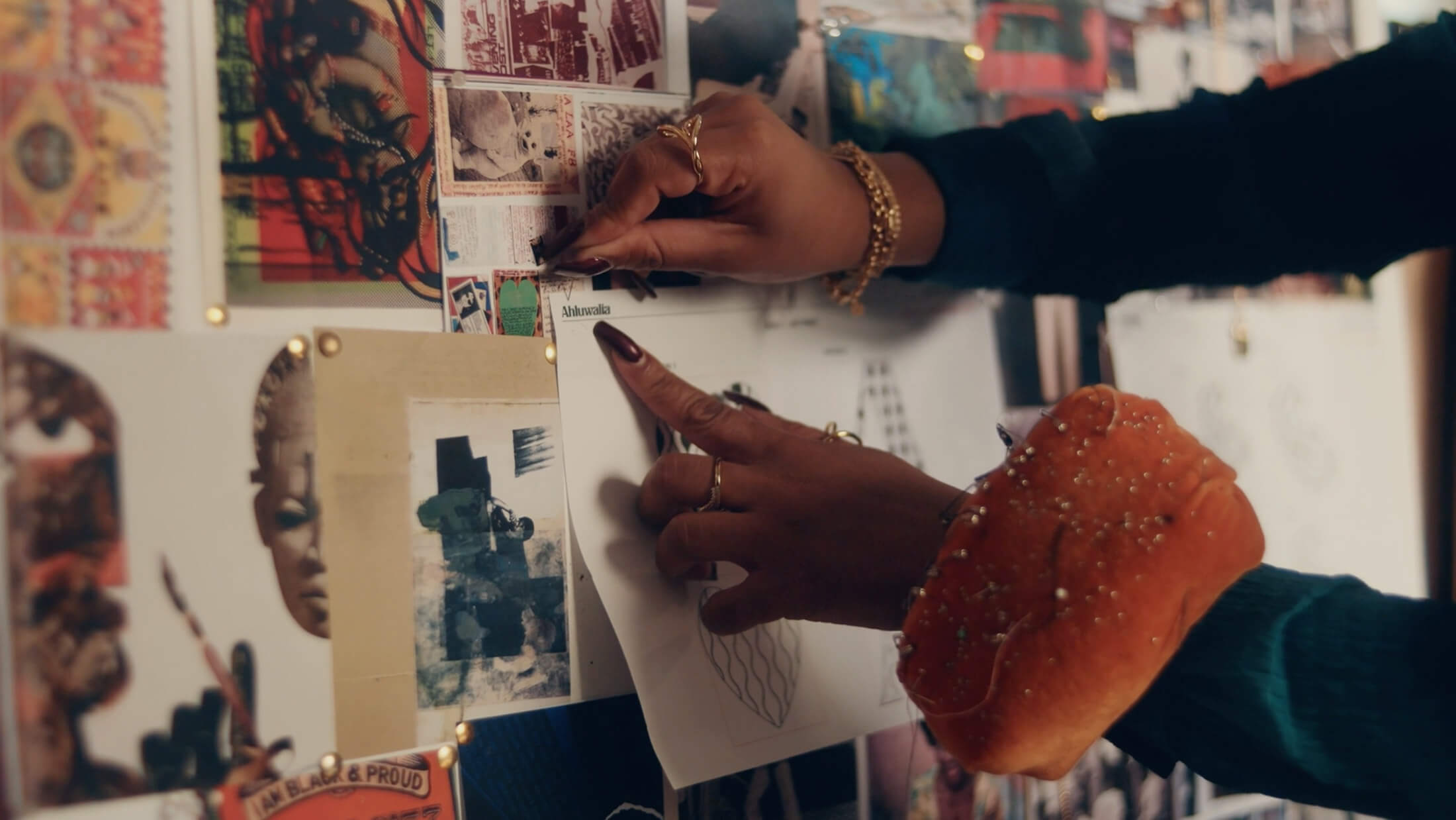 Designer Priya Ahluwalia's hands pinning inspiration on a board on set for Pandora