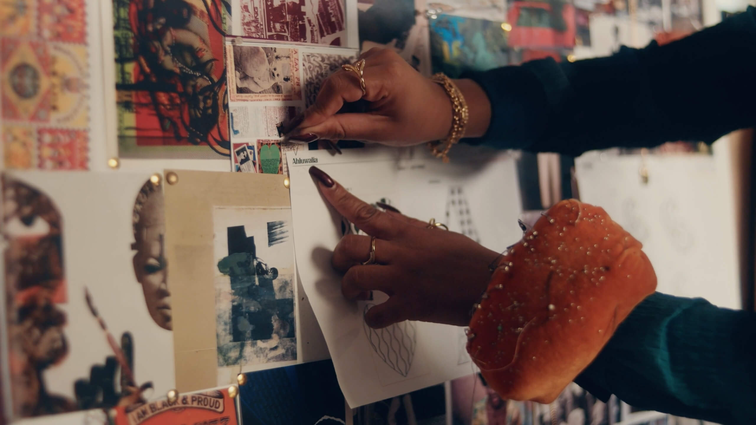 Designer Priya Ahluwalia's hands pinning inspiration on a board on set for Pandora