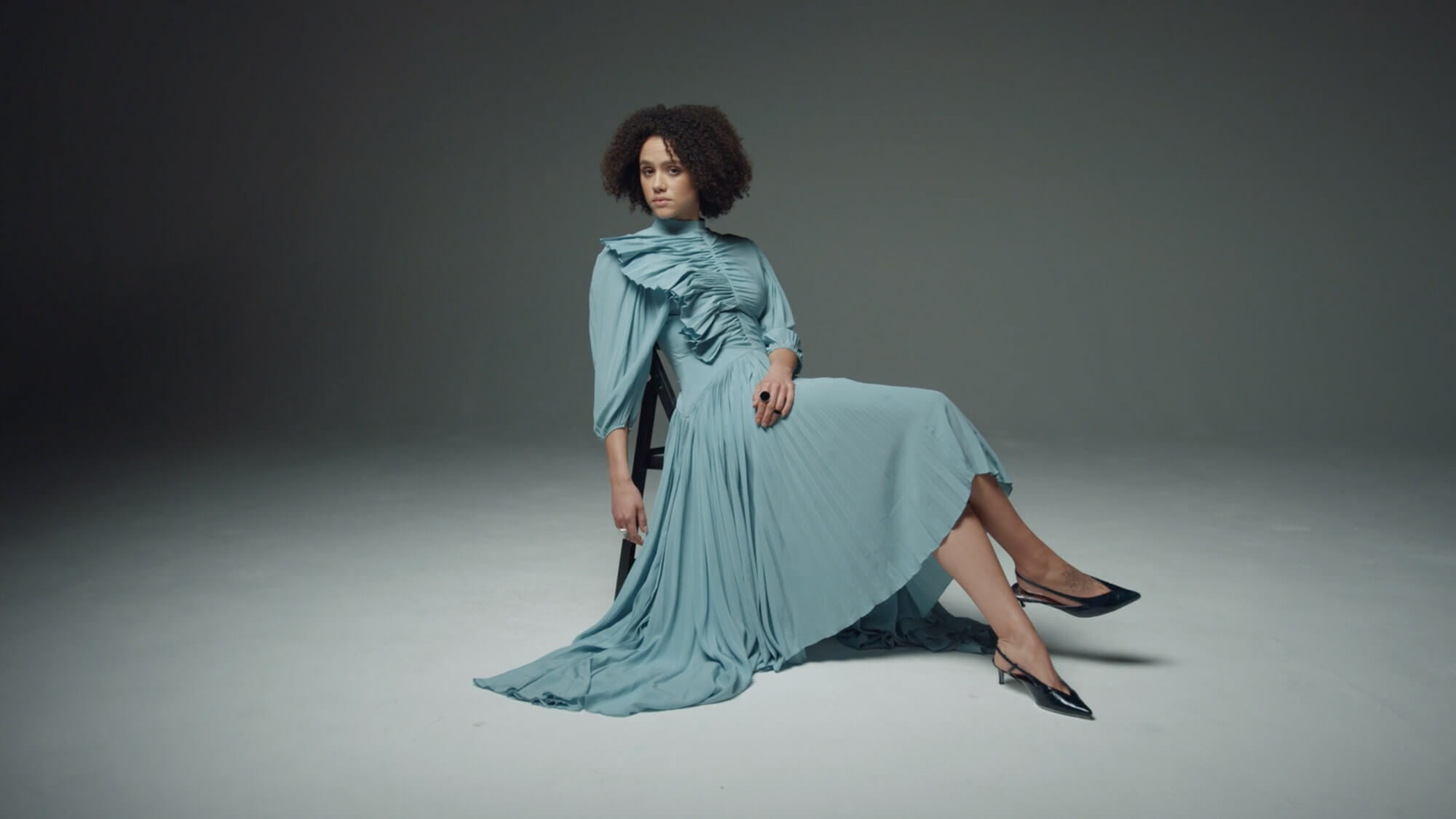 Nathalie Emmanuel sitting on a chair wearing a long blue dress in the Harper's Bazaar film shoot, from the Rise Media case studies archive