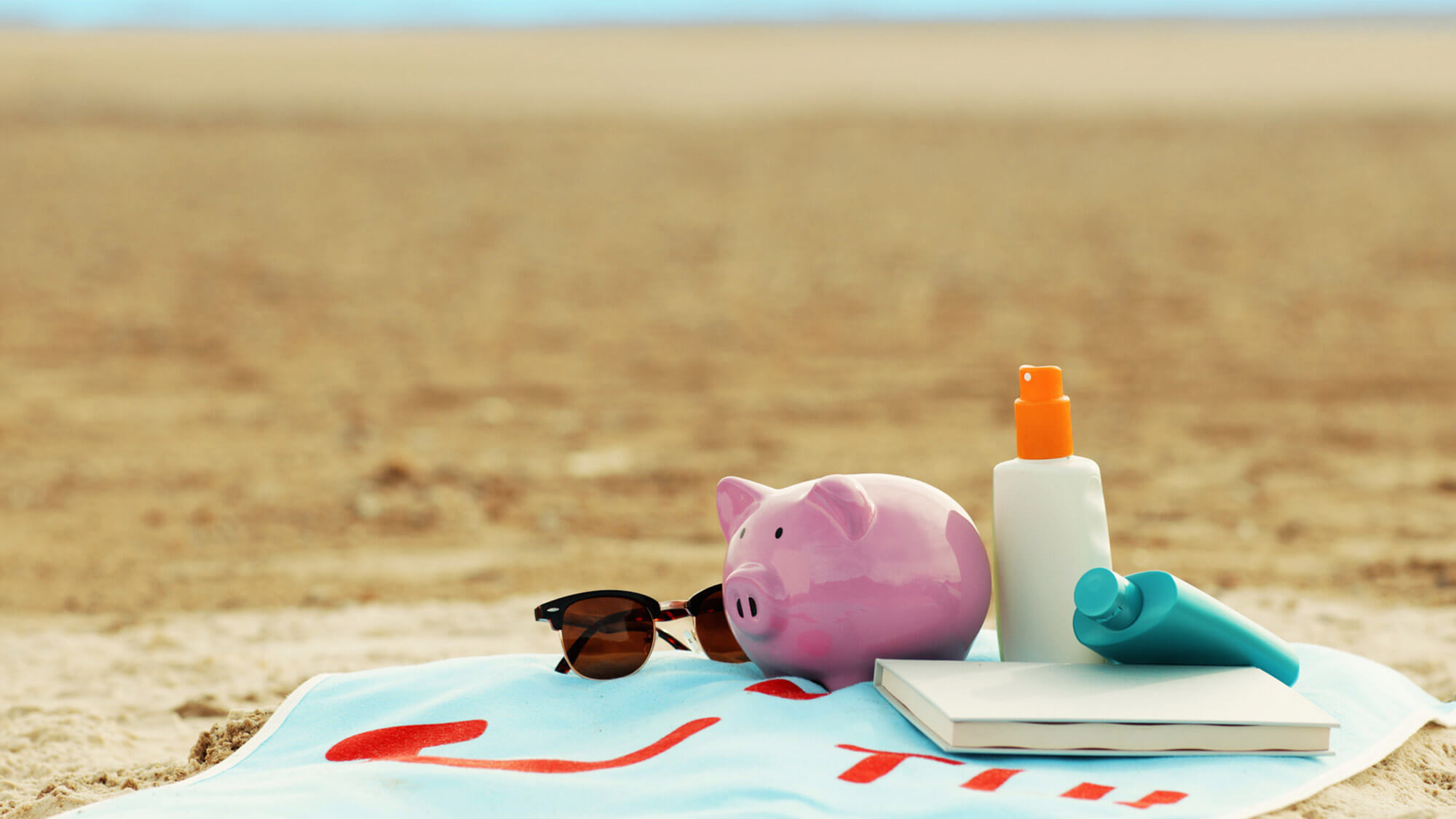 Piggy bank, sunglasses, sun cream and book on a beach towel in our Live Happy video for TUI and The Sun, from the Rise Media case studies archive