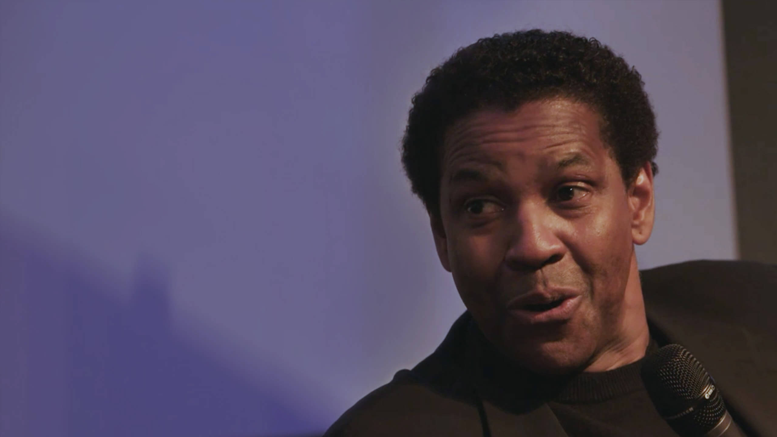 Close-up shot of Denzel Washington in a live interview on stage during a live streaming event