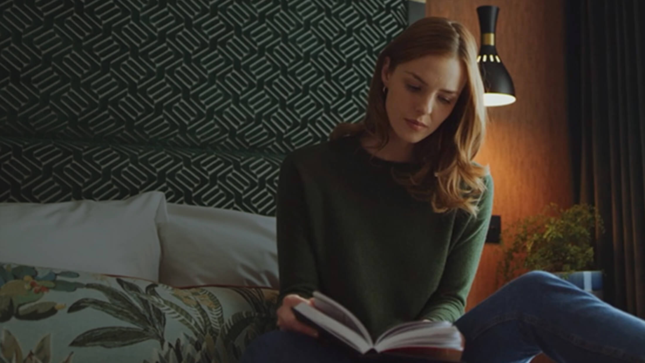 A still image from a property marketing video or property video production, of a woman sat on a bed reading a book in a modern room